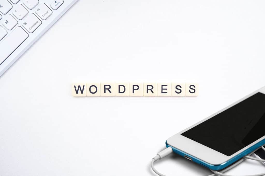 Wordpress written in scrabble tiles on a white desk with phone and keyboard