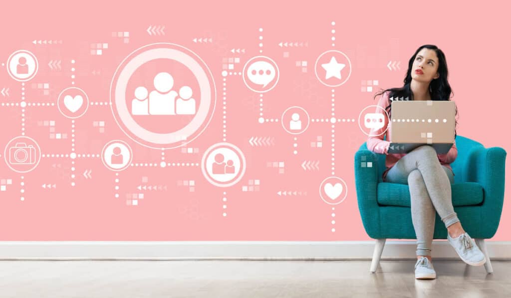 Social Media icons on a pink wall, a girl sitting on a green chair with a computer. She in thinking about her messaging.